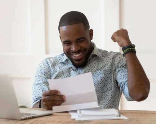 happy African American man looking at a piece of paper next to a laptop.